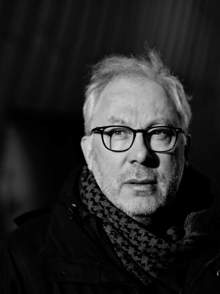 Harmaapartainen henkilö katsoo oikealle mustavalkoisessa kuvassa, yllään silmälasit ja kaulaliina.